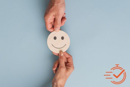 Two hands display a smiley face paper cutout, embodying the joy of coaching and the impact of supportive feedback.