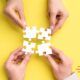 hands holding puzzle pieces on yellow background, symbolizing collaboration skills