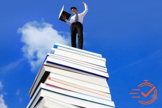 A man stands triumphantly on a pile of books, symbolizing the wisdom and knowledge needed to succeed in business.