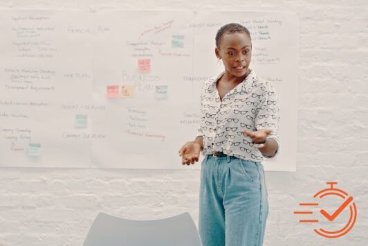 A woman stands confidently in front of a whiteboard, leading a presentation skills training session.