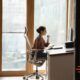 A woman at an ergonomic home office desk, focused, with a window view brightening her workspace.