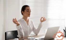A woman sits at her desk, meditating with her laptop, embracing mindfulness in her work environment.
