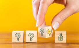 Wooden blocks with a question mark and money symbol are held by a hand, illustrating the problem-solving process
