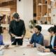 Team members gather at a table with laptops, embodying resilience and collaboration in a dynamic work environment.