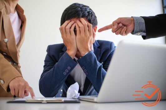 A man sits at a laptop, holding his head in frustration, symbolizing the struggle with workplace bullying.