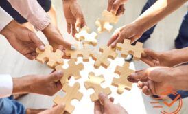 A group of people, holding wooden puzzle pieces, symbolizing collaboration during a corporate teamwork activity.