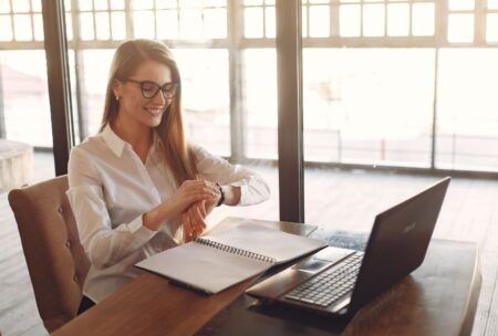a woman with glasses at a table uses her laptop, concentrating on strategies on how to build self discipline