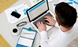 a man focused on his laptop, surrounded by papers and items, working on his personal financial statement