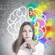 a woman examines a chalkboard displaying a brain, with a colorful rainbow backdrop, as part of her neuromarketing course