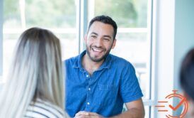 A man smiles warmly at a woman in an office, creating a supportive atmosphere for emotional clients.