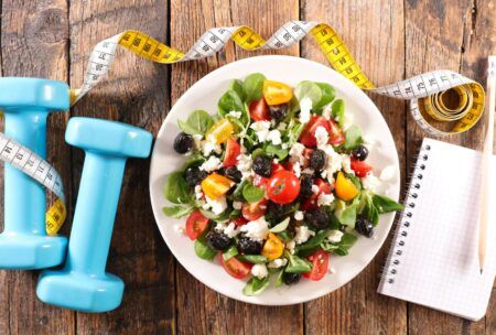 a nutritious salad displayed with blue dumbbells and a notebook, illustrating the concept of a healthy eating course