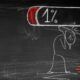 Chalk drawing of a stick figure carrying a large battery icon displaying 1% charge on a blackboard while overcoming burnout.