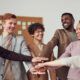 a diverse group of individuals stands united, hands together in front of a board, symbolizing pronouns and intersectionality