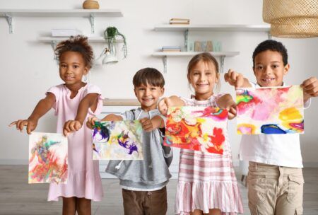 children proudly display their paintings in a room, showcasing their creativity through art therapy for children