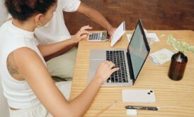 a man and woman discuss debt and credit while seated at a table with a laptop open between them