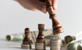 a person strategically places a wooden chess piece atop stacks of money, symbolizing thoughtful purchasing strategies
