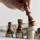 a person strategically places a wooden chess piece atop stacks of money, symbolizing thoughtful purchasing strategies