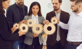 business professionals collaboratively holding wooden gears, symbolizing effective delegation in management practices