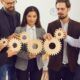 business professionals collaboratively holding wooden gears, symbolizing effective delegation in management practices