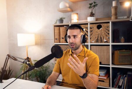 A podcast beginner in a yellow shirt speaks into a microphone, engaged in a podcasting session.