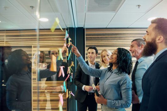 team members examining sticky notes on a glass wall as part of a user stories course activity