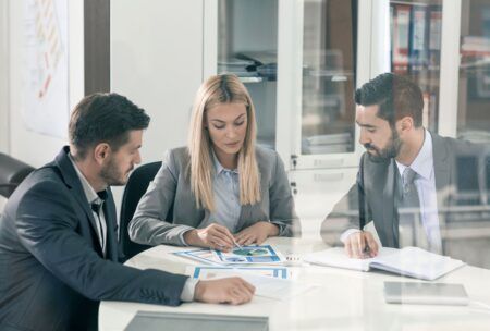 three business professionals seated at a table, reviewing documents related to business sustainability practices