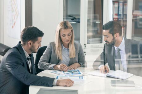 three business professionals seated at a table, reviewing documents related to business sustainability practices
