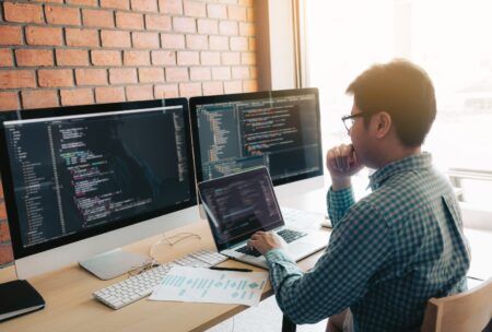 a man at a desk with dual computer screens, engaged in developing a chatbot using Python programming