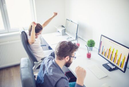 Two people at a desk with arms raised, celebrating success in a beginner's guide to Excel workshop.