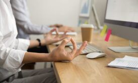 A woman meditates in front of a computer, promoting health and wellness in the workplace.