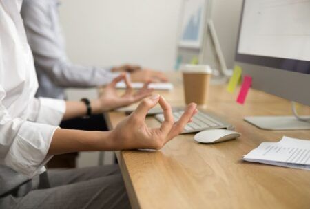 A woman meditates in front of a computer, promoting health and wellness in the workplace.