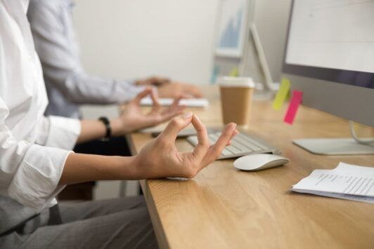 A woman meditates in front of a computer, promoting health and wellness in the workplace.