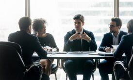 A group of business professionals discussing operating cadence around a conference table.