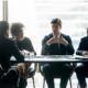A group of business professionals discussing operating cadence around a conference table.
