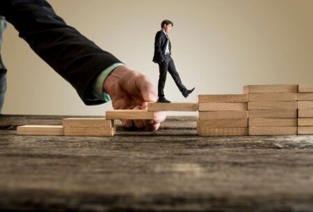 businessman stepping on wooden blocks to climb a ladder, symbolizing overcoming obstacles in his career journey