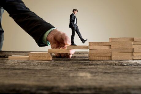 businessman stepping on wooden blocks to climb a ladder, symbolizing overcoming obstacles in his career journey