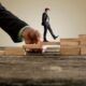 businessman stepping on wooden blocks to climb a ladder, symbolizing overcoming obstacles in his career journey