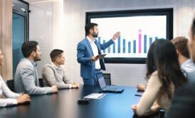 A man in formal attire presents to a group, highlighting the various types of meetings in a business context.