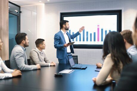 A man in formal attire presents to a group, highlighting the various types of meetings in a business context.
