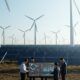 Three individuals stand before wind turbines, symbolizing sustainable finance and renewable energy solutions.