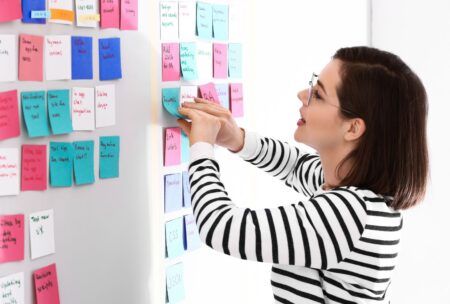 a woman organizes sticky notes on a whiteboard as part of her agile project management certification training