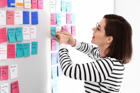 a woman organizes sticky notes on a whiteboard as part of her agile project management certification training