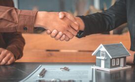 two people shaking hands over a house model, symbolizing a discussion on buying vs renting a home