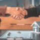 two people shaking hands over a house model, symbolizing a discussion on buying vs renting a home