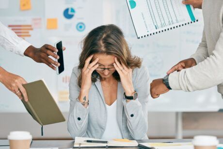 a woman holds her head in her hands, surrounded by others, symbolizing the struggle from burnout to balance