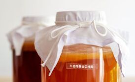 two jars of liquid covered with white cloths, demonstrating how to brew kombucha