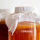 two jars of liquid covered with white cloths, demonstrating how to brew kombucha
