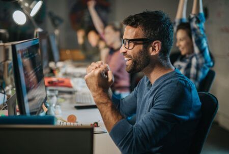 a man wearing glasses sits at a desk with his hands raised, engaged in a kivy python tutorial