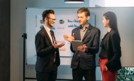 three business professionals collaborate around a table, reviewing a tablet related to project management courses
