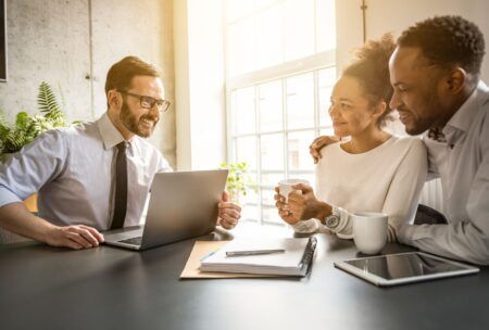 Three people gathered around a table with a laptop, focused on understanding life insurance basics.